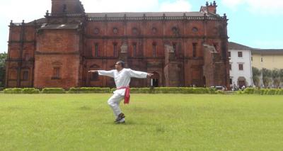 A man holds his arms out for a pose on the grass in front of an enormous old mansion.