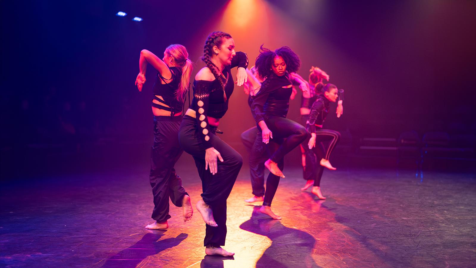 several people wearing black costumes on stage with orange and purple lights