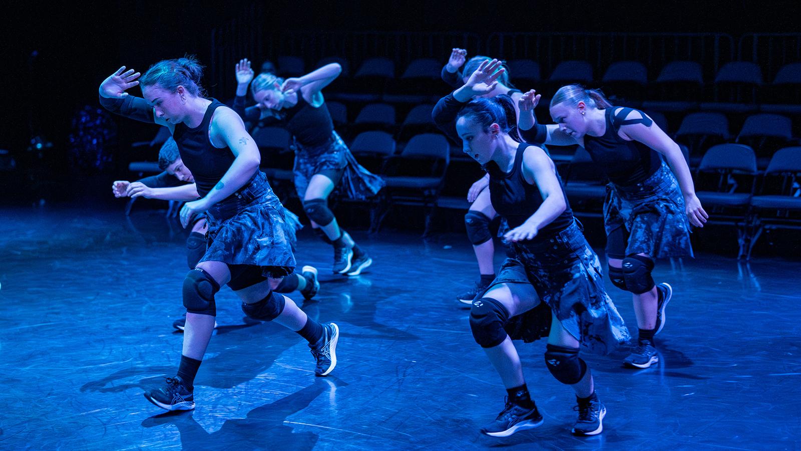 dancers wearing kilts and black tank tops on a lit stage